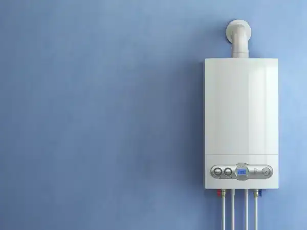 A modern white tankless water heater is mounted on a smooth light blue wall, featuring front control buttons and display, with pipes connected underneath—expertly installed by an HVAC Contractor North Attleboro.