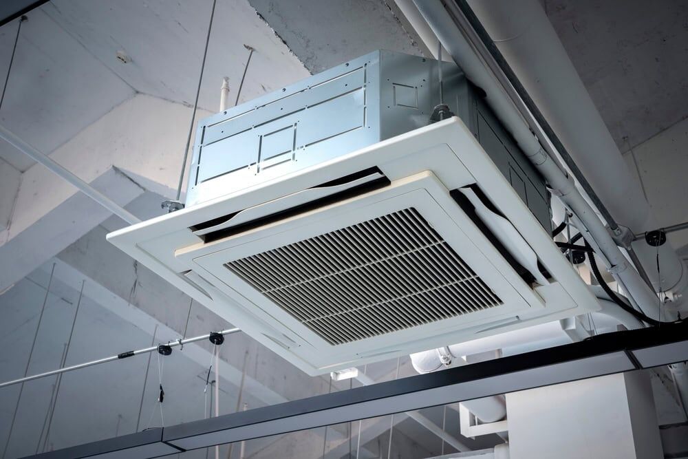 A close-up view of a ceiling-mounted air conditioning unit in an industrial-style building with exposed pipes and ductwork, showcasing quality AC Installation North Attleboro by a trusted HVAC contractor.