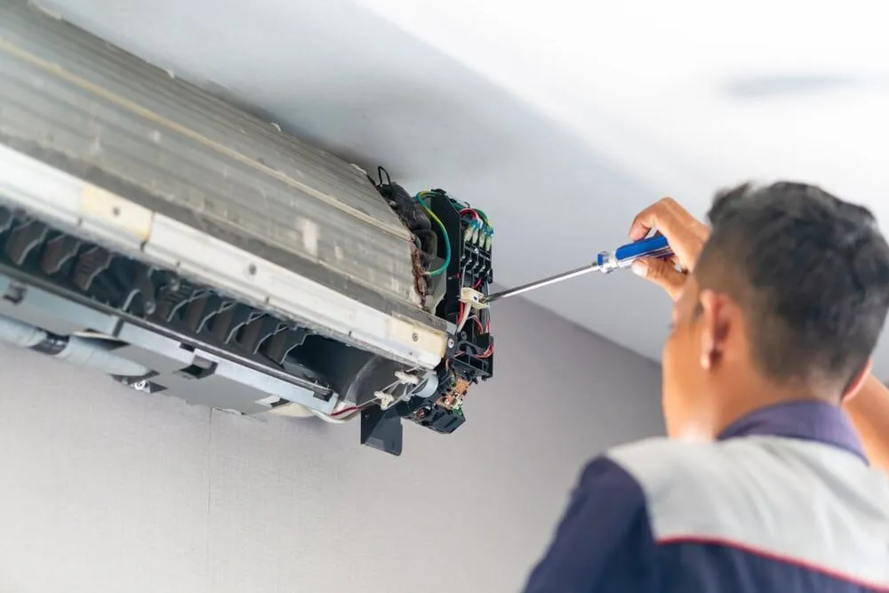 A technician uses a screwdriver to repair or maintain the internal components of a wall-mounted air conditioning unit, providing expert AC Services North Attleboro, MA residents can trust.