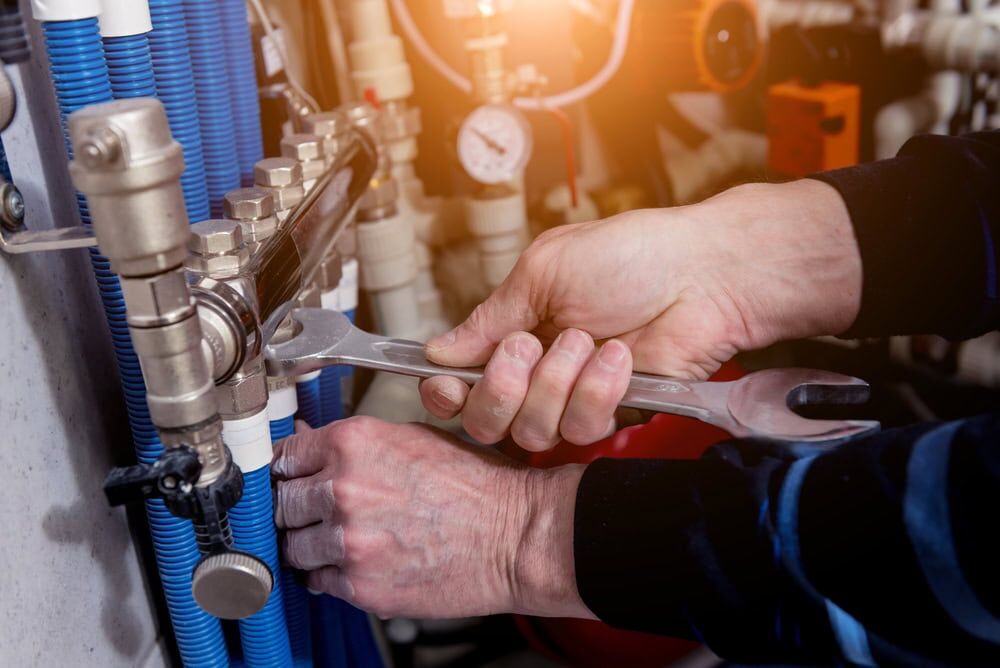 Close-up of a person’s hands using a wrench to tighten a fitting on a complex system of pipes and valves, with blue and white tubing and pressure gauges—typical work for an HVAC Contractor in North Attleboro, MA.