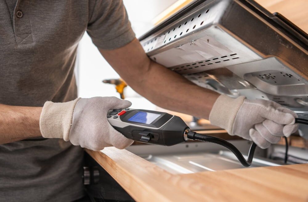 A person wearing gloves uses a handheld inspection camera to examine the inside of an open kitchen oven, demonstrating the attention to detail you’d expect from a top HVAC Contractor North Attleboro, MA.