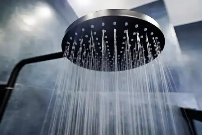 A black overhead rain shower head with multiple water streams cascading down. The background is blurred, giving a sense of a modern, dark-tiled bathroom.