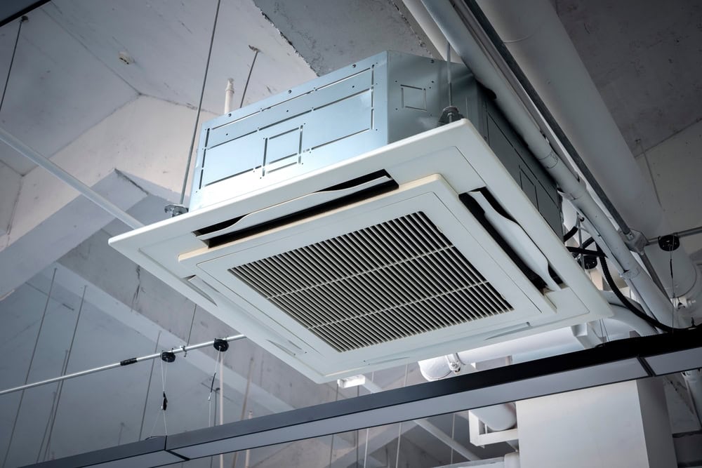 A close-up view of a modern ceiling-mounted air conditioning unit with metal ducts and pipes visible in an industrial-style interior.