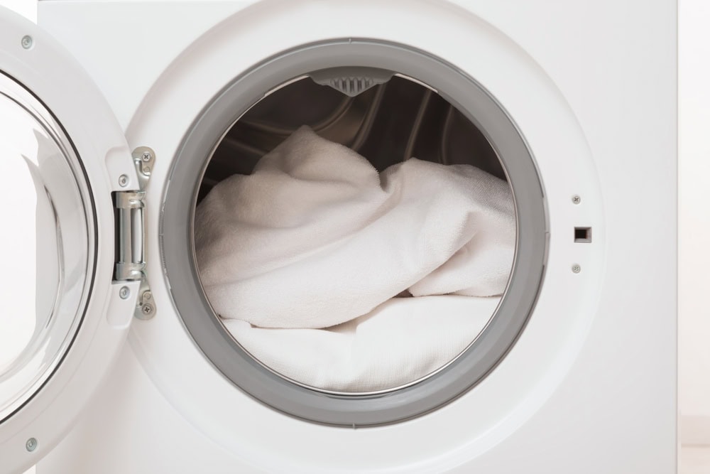Front-loading washing machine with its door open, showing several white towels or clothes inside the drum, ready to be washed.