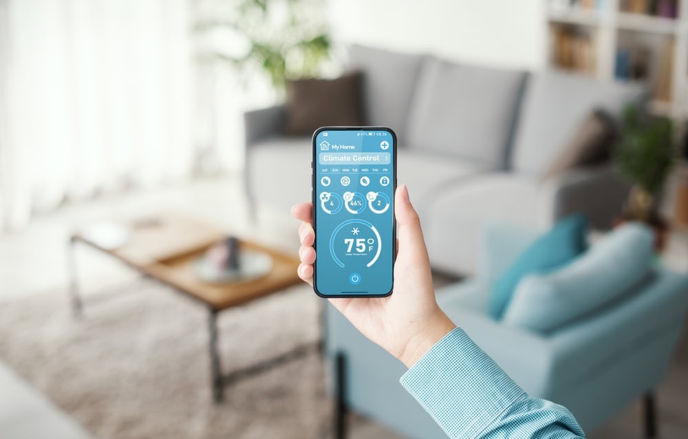 A person holds a smartphone displaying a climate control app set to 75°F in a bright, modern living room—perfect comfort thanks to expert AC services in North Attleboro.