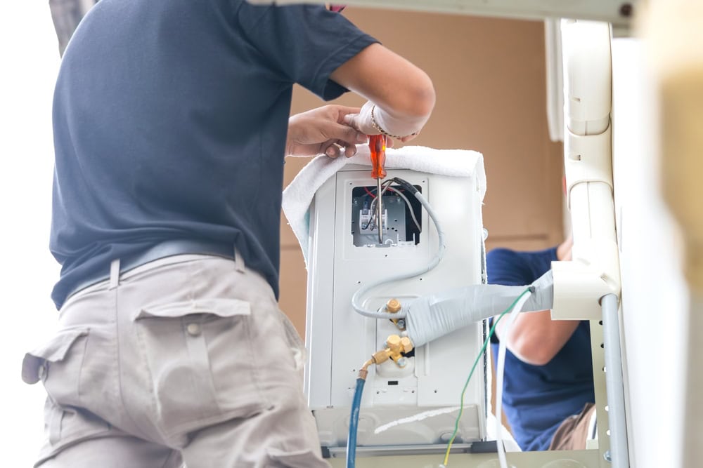 HVAC technician performing air conditioner repair and maintenance, wearing uniform with tools, servicing a home unit in North Attleboro, MA for Dempsey Energy